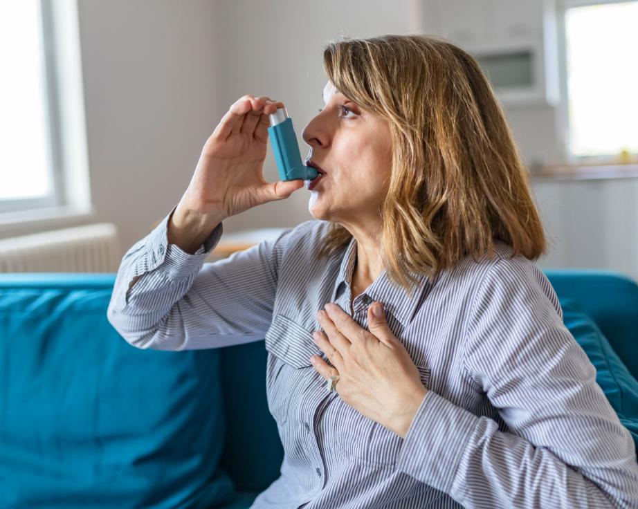 Woman using an asthma inhaler on a couch