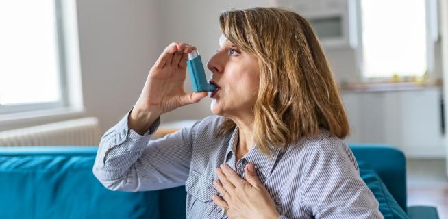 Woman using an asthma inhaler on a couch