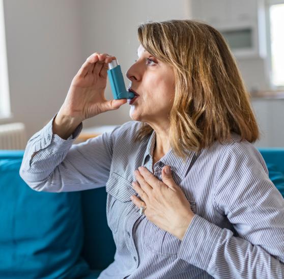 Woman using an asthma inhaler on a couch