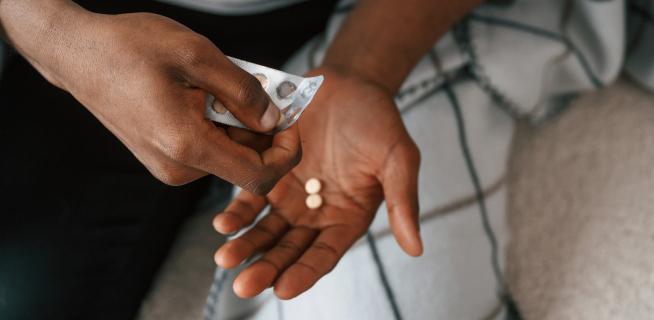 Close-up of a person holding a blister pack and taking two pills from it, used for genital herpes treatment.