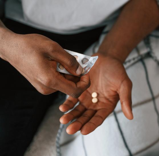 Close-up of a person holding a blister pack and taking two pills from it, used for genital herpes treatment.