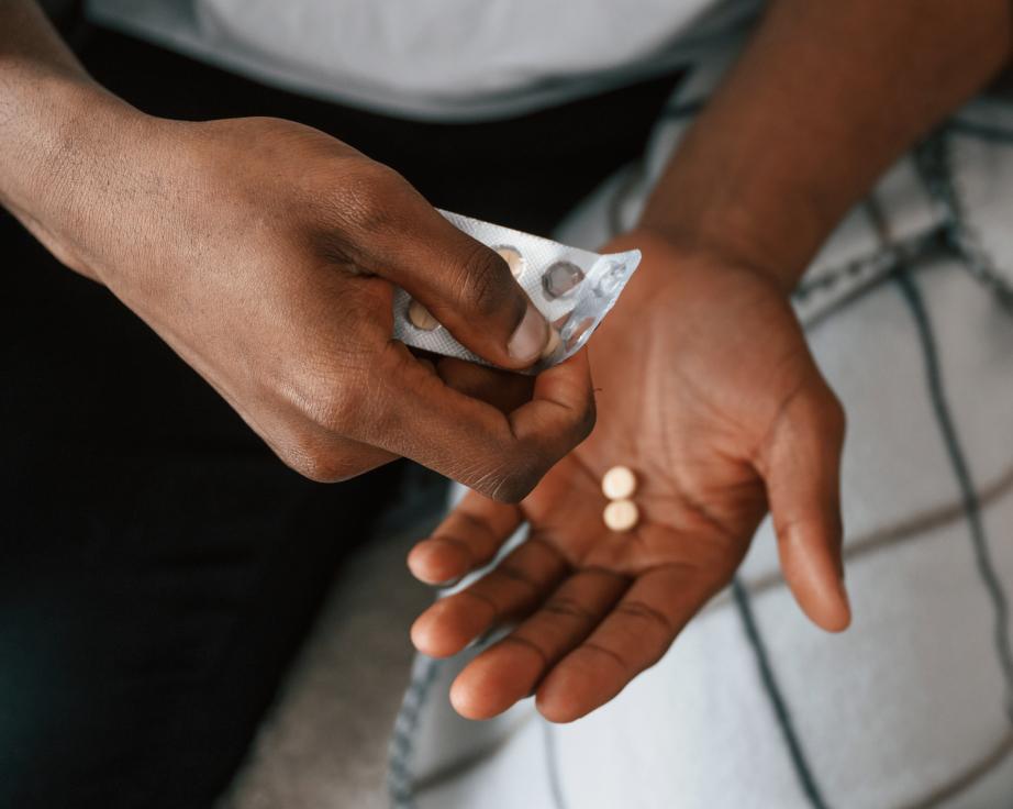 Close-up of a person holding a blister pack and taking two pills from it, used for genital herpes treatment.